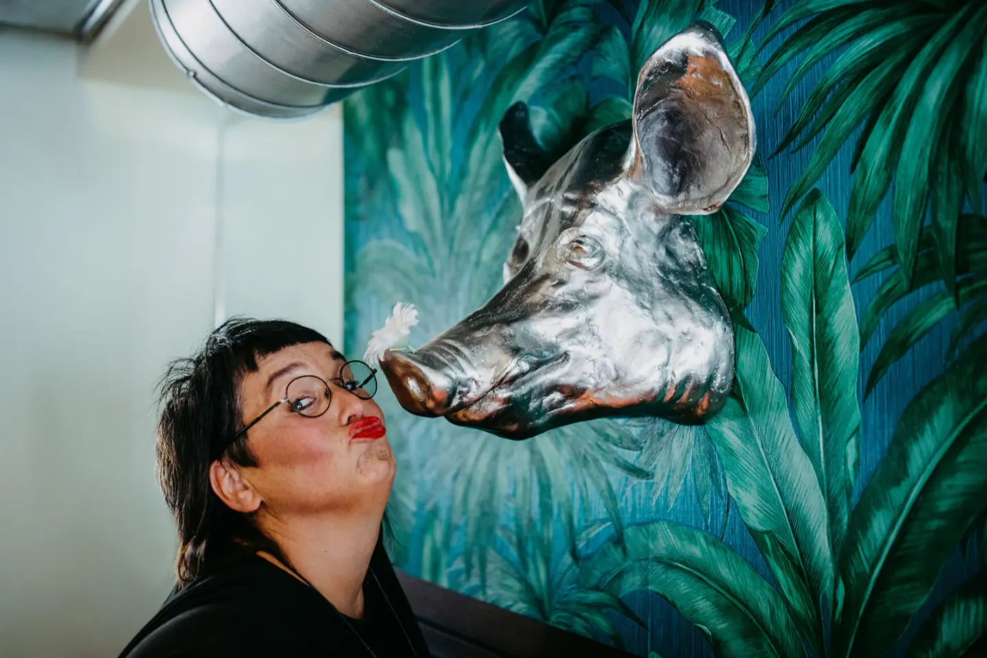 Sabine Jung-Bass küsst Wildschwein-Skulptur vor Pflanzenwand auf der Suche nach Glück