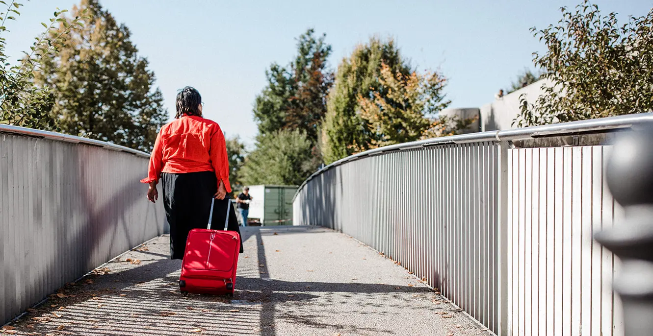 Sabine Jung-Bass die mit rotem Koffer auf Brücke spaziert
